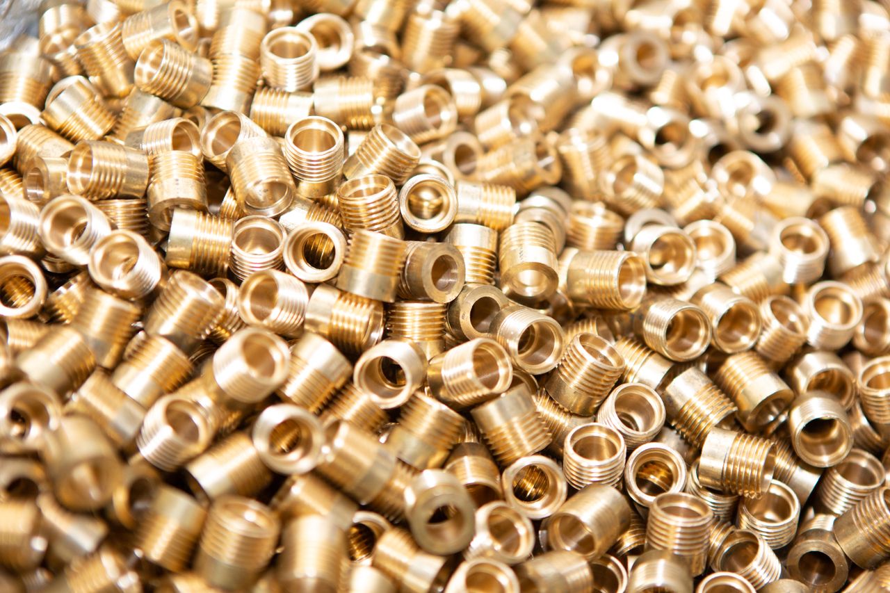Services A detailed close-up of a pile of brass screws and nuts with a golden metallic finish.